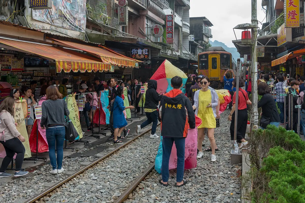 Visitants sostenint grans fanalets celestes de paper pintat a les vies de tren del carrer vell de Shifen, amb un tren esperant al fons
